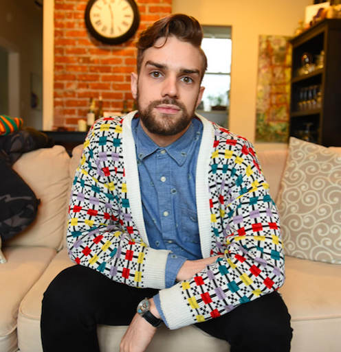 Gay San Francisco Ballet dancer Myles Thatcher poses with a colorful cardigan in his living room, with exposed brick in the back.