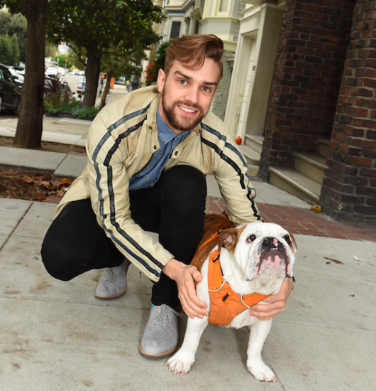 Dancer Myles Thatcher poses in a San Francisco street with a bulldog that is wearing an orange harness.