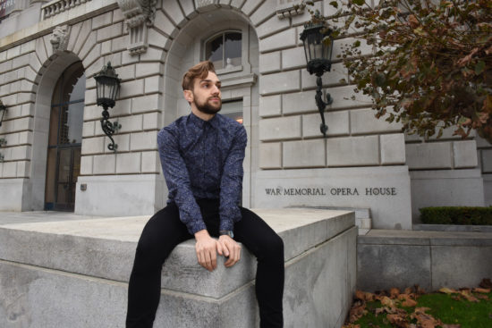 Myles Thatcher poses in a blue sweater in front of the War Memorial Opera House in San Francisco.